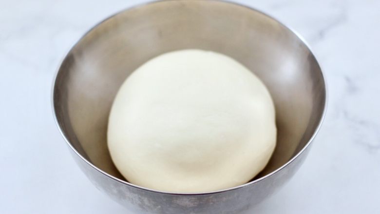 德式热狗面包,把面团取出揉圆后，盖上保鲜膜，放入烤箱的发酵模式里进行发酵。
