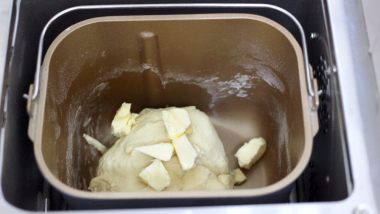 德式热狗面包,启动和面一个程序后，看见面团能扯出粗膜时，加入室温软化的黄油，再次启动面包机，进行一个和面程序。