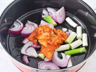 部队火锅,锅中倒入适量的食用油烧热，放入大葱、洋葱、辣白菜