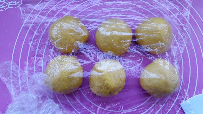 南瓜豆沙面包,按压面团排气后，平均分割成6个小面团，盖保鲜膜醒发15分钟。