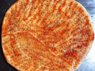 虾仁培根披萨,在披萨饼底上刷上一层番茄沙司、撒上一些披萨草。