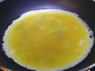 秋葵厚蛋烧,倒入四分之一蛋液，晃动平底锅，摊平蛋液。