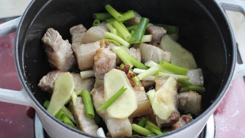 梅干菜烧肉,接着放入冰糖翻炒融化，再放葱段、姜片、八角和香叶炒出香味。