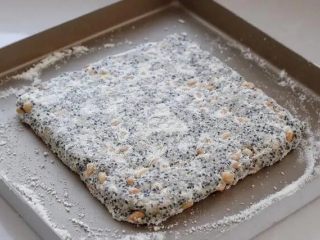 芝麻花生糖,将翻拌好的混合物取出放进烤盘中，借助刮板按压整理成有一定厚度的正方形。