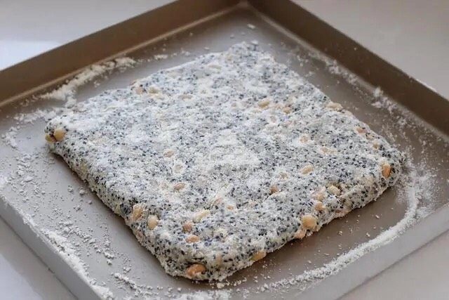 芝麻花生糖,将翻拌好的混合物取出放进烤盘中，借助刮板按压整理成有一定厚度的正方形。