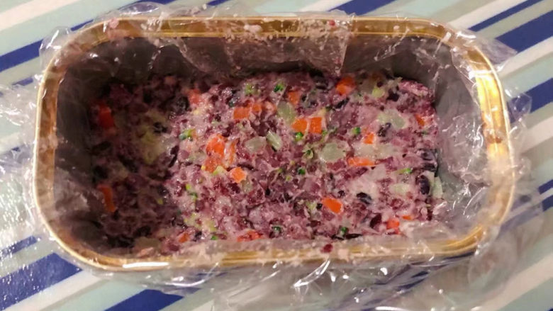 紫米饭团,保鲜膜先放入午餐肉盒中再取适量拌好的时蔬双米饭压实