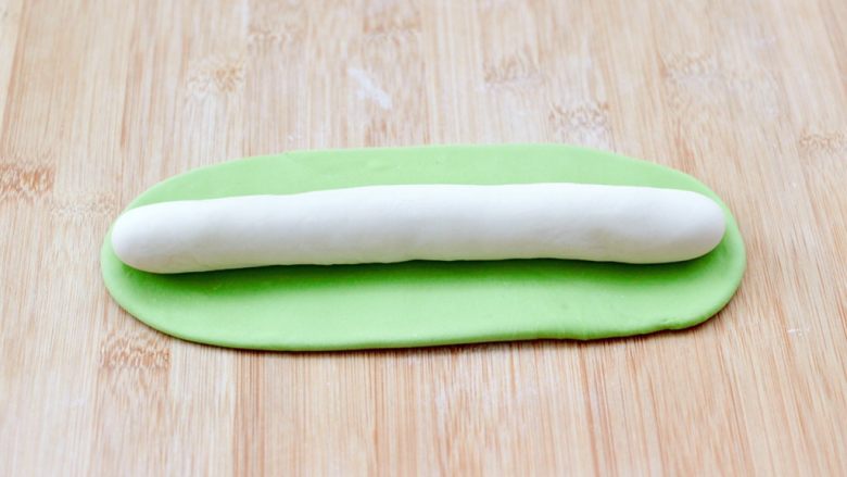 海蛎子肉丁萝卜饺子,把面团揉匀，白色的搓成长条，绿色的擀成面皮，白色的放到上面，用绿色的面皮包裹起来搓成长条。