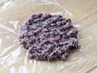 紫米饭团,案板上先铺一层保鲜膜，再舀取适量紫米饭放到上面摊开。