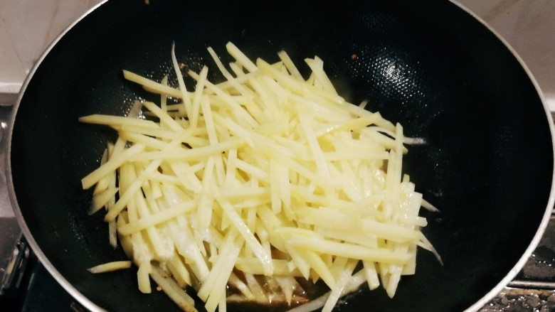 青椒炒土豆丝,锅中留下底油和八角继续加热，放入土豆丝翻炒。