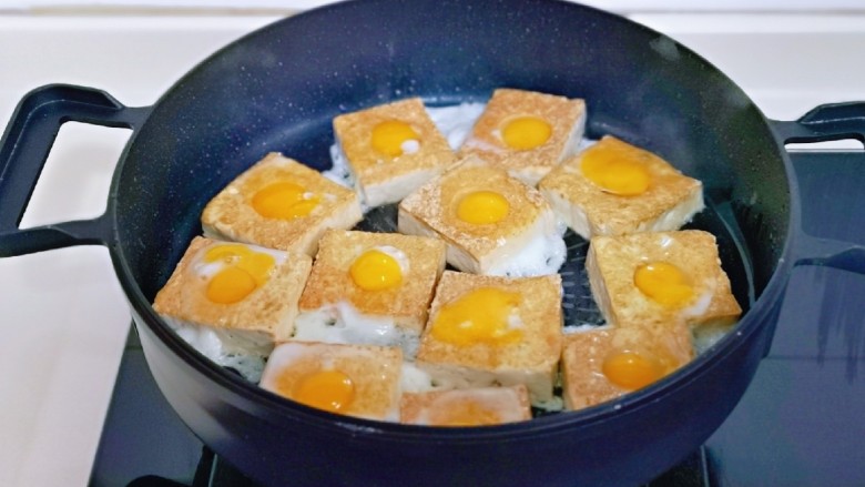 茄汁鹌鹑蛋,待底部煎至金黄时将豆腐翻面，这时把鹌鹑蛋磕入圆圈中，保持小火煎至。