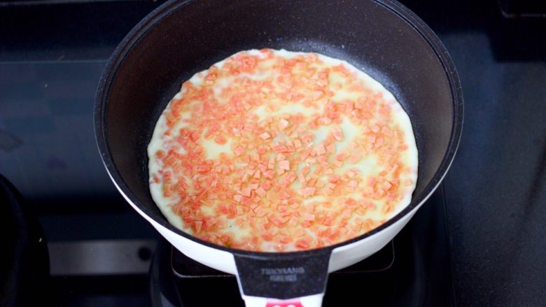 日式火腿鸡蛋卷,平底锅刷一次薄薄的油，先倒入蛋清火腿粒摊匀摊平。