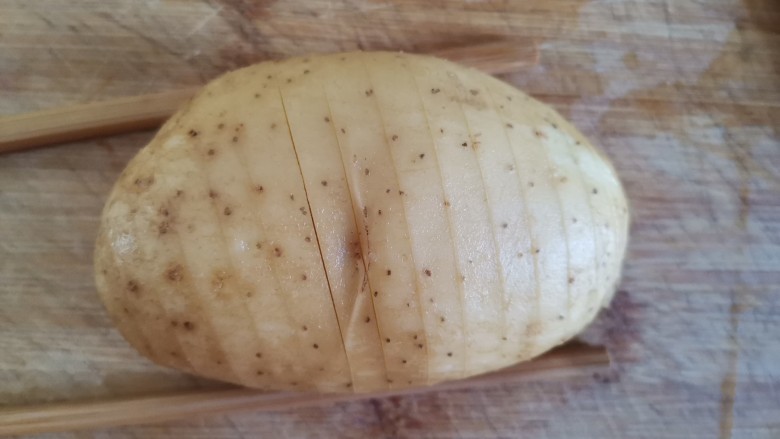 风琴烤土豆,把2个筷子放在土豆两边，用刀切土豆切成5毫米厚，不要切到底