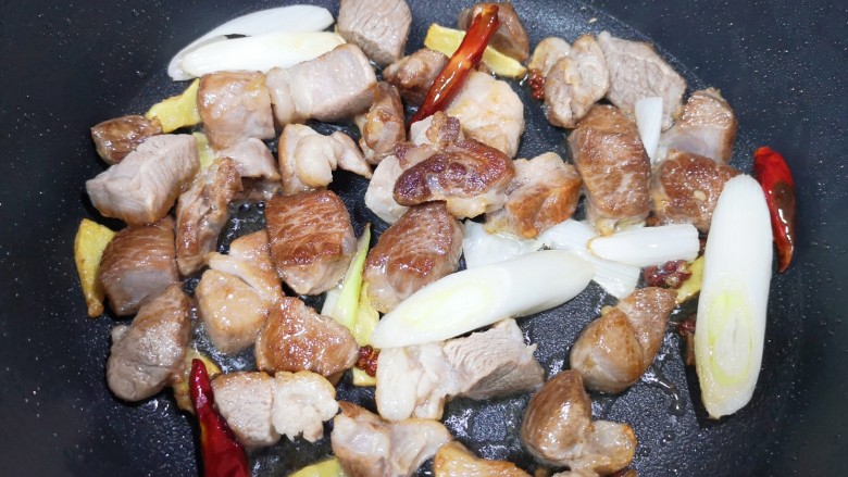 红烧羊肉,下入葱段、干红辣椒和花椒，翻炒至羊肉微微出油。 