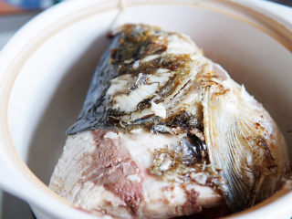 鱼头豆腐煲,焖锅底部放入一些姜片、从短裙，防粘锅底，将煎制好的鱼头放入焖锅内。