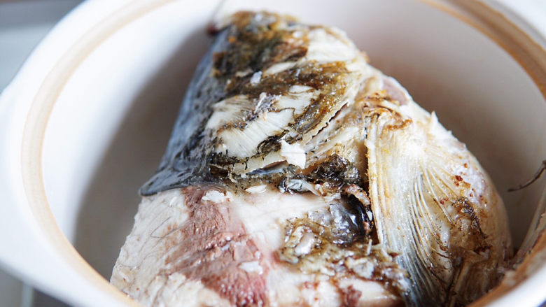 鱼头豆腐煲,焖锅底部放入一些姜片、从短裙，防粘锅底，将煎制好的鱼头放入焖锅内。
