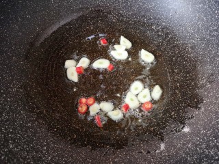 黄瓜炒腊肠,煎腊肠的余油继续加热，下入蒜片和小米椒炒出香味。