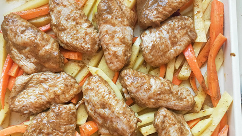 孜然烤鸡翅,在烤盘上先铺满土豆条和胡萝卜条，上面放上腌制好的鸡翅