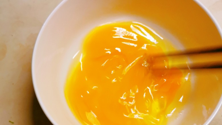 香椿炒蛋,鸡蛋敲入碗中打散。