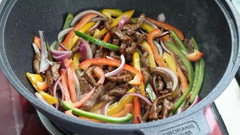 黑椒牛肉意面,就锅中底油放入彩椒和洋葱，快速翻炒一分钟，倒入炒好的牛肉混合翻炒均匀。