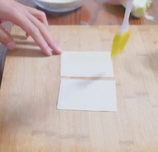 煎饼果子,步骤二：将两块抄手皮沾一丢丢水叠在一起，用擀面杖擀薄。下锅炸制酥脆。