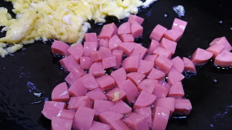 鸡蛋火腿炒饭,鸡蛋推到锅边，放入火腿丁，文火煎出香味。