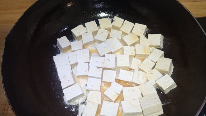 韭菜豆腐,倒入豆腐煎炸，将豆腐平铺，煎至一面金黄后