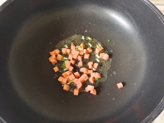 彩蔬火腿丁,炒锅中加入适量花生油烧热，放入葱花爆香，加入火腿肠粒翻炒均匀