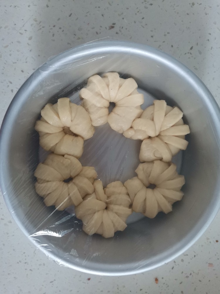 奶香小面包,捏住两头使之弯曲，依次放入6寸圆形的模具里，放在温暖的地方进行二次发酵