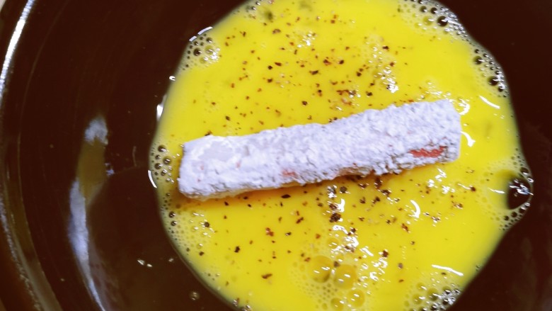 酥炸蟹柳,取一条蟹柳放入淀粉中，包裹上淀粉后，放入蛋液中，包裹一层蛋液。