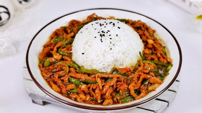 青椒肉丝盖浇饭,盘子中间扣一碗米饭，撒芝麻，盛入青椒肉丝。