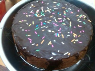 巧克力淋面蛋糕,把可可戚风蛋糕放在晾架上,放进盆里,趁温热时把酱淋在蛋糕表面.再撒上彩色巧克力针.