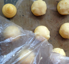 脆皮菠萝泡芙,揭开一面的塑料袋，将面片盖在泡芙糊上，再轻轻揭下另一面的塑料袋，完成的泡芙坯，入提前预热的烤箱烘焙。
