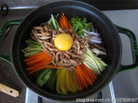 铸铁锅版石锅拌饭,码上各色蔬菜，鸡肉丝一半放在边上，一半放在中间，在鸡肉上打一个生鸡蛋；