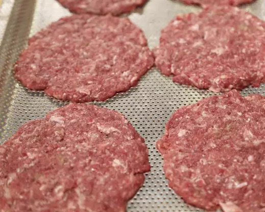 芝士酱牛肉汉堡,肉摊成约厚5毫米的饼状，烤盘刷上一层油后放上牛肉饼，撒上适量食盐。放入烤箱约3分钟。