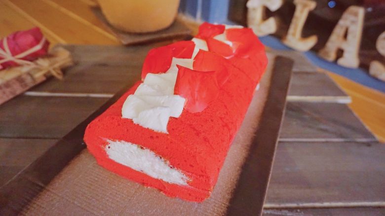 红丝绒蛋糕卷,最后，在蛋糕卷上挤上奶油，用玫瑰花或其它东西点缀一下，美美的红丝绒卷就完成啦！放进冰箱冷藏一下会更美味哦！