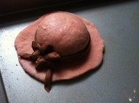粉嫩帽子面包,可可面团剩余部分搓成细长条，围在上一步圆面团周围，将小花点缀上去，完成帽子造型。