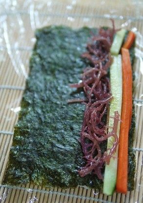 海草寿司,放入胡萝卜条、<a style='color:red;display:inline-block;' href='/shicai/ 54'>黄瓜</a>条、血珊瑚草，一边卷，一边把寿司帘和保鲜膜往前拉，不要一起卷进去。