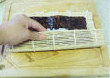 寿司拼盘,左手拇指与食指提起海苔与寿司帘的底部，其他指头挡住寿司里的食材防止掉出