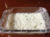 剩饭做米糕,方形的容器中铺上保鲜膜，将米饭倒入其中，用勺子背面将米饭压紧、铺平。然后放入冰箱冷藏