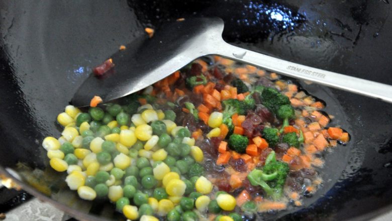 芝士焗香肠时蔬土豆泥,倒入焯过水的青豆和玉米，加少量盐，继续翻炒。