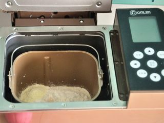 淡奶油椰蓉面包卷,将面粉及奶粉覆盖在液体之上，对角分别上放上盐和糖A，在面粉中间挖一个小坑，放上酵母，启动面包机揉面程序20分钟。