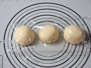 淡奶油椰蓉面包卷,将面团取出，按揉排气后面团均分成三团，盖上保鲜膜松弛15分钟。
