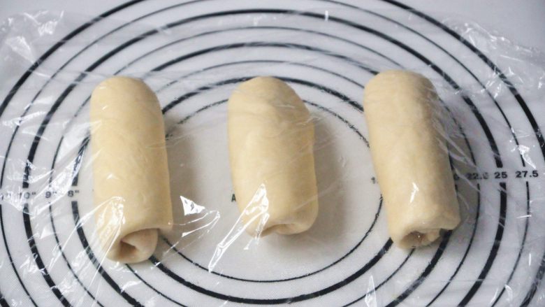 淡奶油椰蓉面包卷,将面团擀开卷成圆筒状，3个都做同样处理，盖上保鲜膜静置15分钟左右。