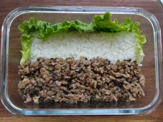 小兔子拔萝卜—儿童营养便当,在饭盒的一侧垫上一片洗净的生菜叶，然后将米饭装入饭盒中，中间铺一片切达早餐奶酪片，上面再铺上米饭，压平。
