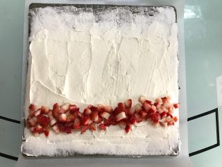 黑米戚风蛋糕卷,将奶油抹在蛋糕表面，起始端稍厚，尾部稍薄并留空一些不要抹奶油，放上草莓。