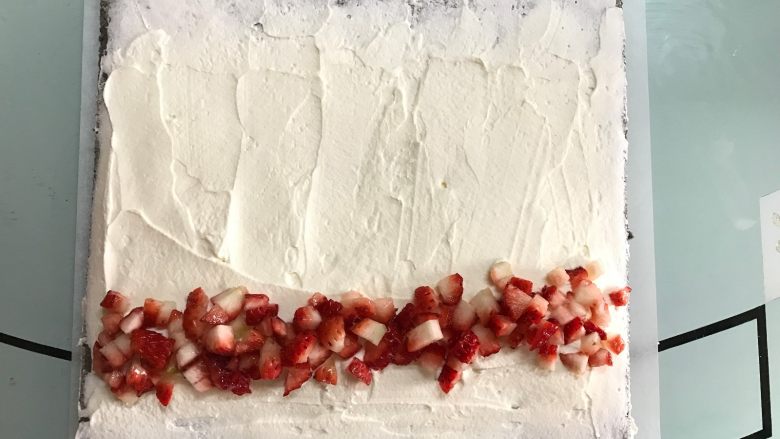 黑米戚风蛋糕卷,将奶油抹在蛋糕表面，起始端稍厚，尾部稍薄并留空一些不要抹奶油，放上<a style='color:red;display:inline-block;' href='/shicai/ 592'>草莓</a>。