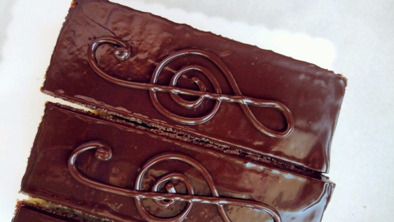 欧培拉歌剧院蛋糕,剩的镜面巧克力装入裱花袋，剪小口，表面凝固后画上音符图案，用少许金箔和可食用金粉装饰即可