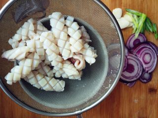 洋葱炒鱿鱼,入七八十度的热水中，快速焯一下，看到鱿鱼微微卷起立刻捞出，沥净水分。切洋葱，葱花和胡萝卜丝