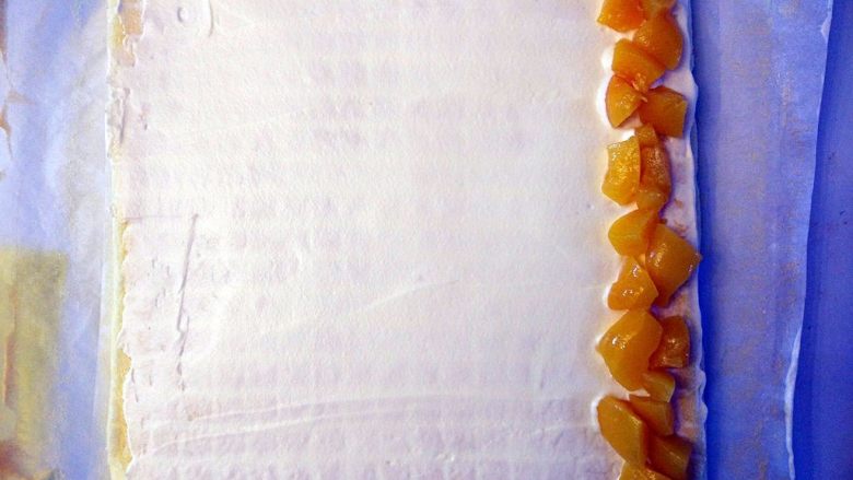黄桃奶油蛋糕卷,将蛋糕体放在油纸上，表面抹少许淡奶油，将切碎的黄桃快铺在一边，在图中黄桃块左边再抹少许奶油，形成一个坡度，这样卷起后不会有空隙