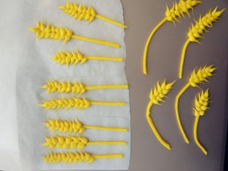 阳光麦田创意面食,将一块黄色面团擀成薄片，切细条，将搓成雨滴状带尖端的面团左右依次黏在上面，做成麦穗的样子